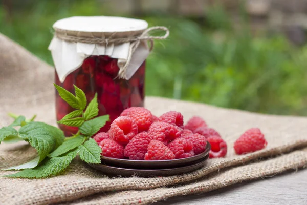 Raspberry preserve in glass jar and fresh raspberries on a plate — Stock Photo, Image