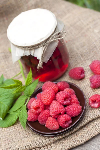 Raspberry preserve in glass jar and fresh raspberries on a plate — Stock Photo, Image