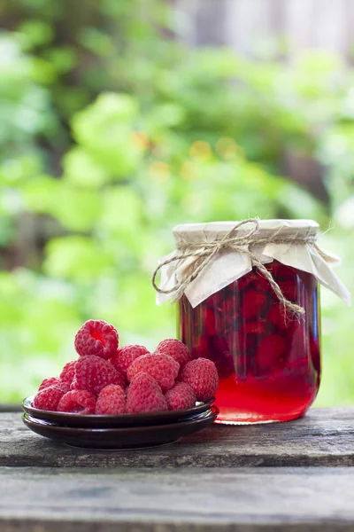 Raspberry preserve in glass jar and fresh raspberries on a plate — Stock Photo, Image