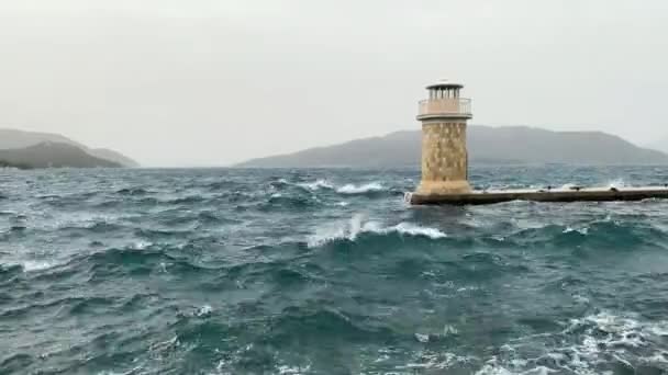 Waves break on the city embankment with a small breakwater and a lighthouse. Stormy weather. — Stock Video