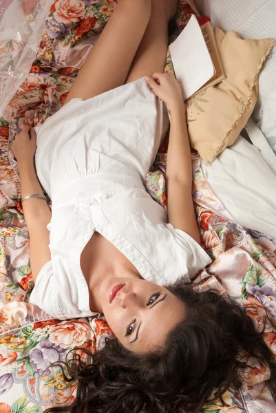 Młoda brunetka, leżąc na łóżku z książki i marzenia — Zdjęcie stockowe