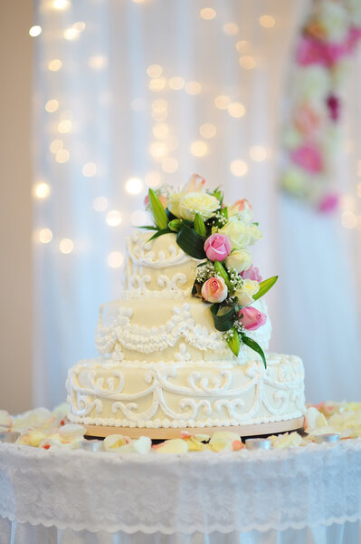 A multi level white wedding cake on a silver base and pink flowers on top