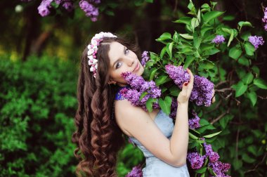 Beautiful young woman in lilac flowers, outdoors portrait
