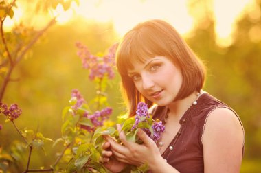 Beautiful young woman in lilac flowers, outdoors portrait