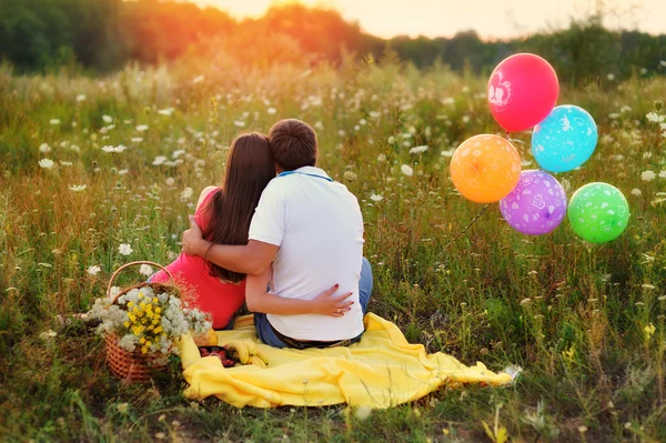 Man and woman sitting in the field and colorful balloons — Stock Photo, Image