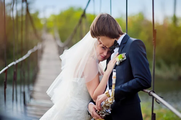 Unga lyckliga bruden och brudgummen står på en bro medan bruden pekar på copyspace — Stockfoto