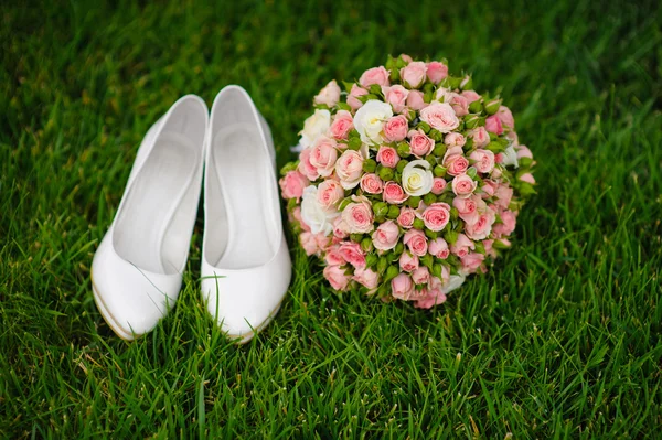 Bridal bouquet and white female shoes on grass — Stock Photo, Image