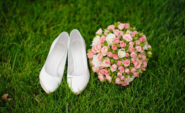 Wedding bouquet and shoes lying down on green grass — Stock Photo, Image