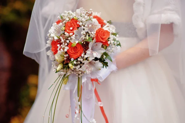 Νύφη, κρατώντας μια γαμήλια ανθοδέσμη με κόκκινα και άσπρα λουλούδια — Φωτογραφία Αρχείου