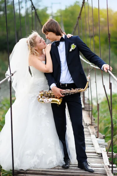 Bride and groom on the bridge with a saxophone — Stock Photo, Image