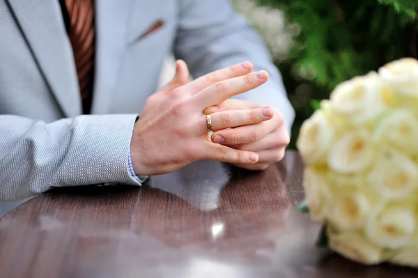 El novio está sentado en la mesa y retuerce el anillo en su dedo. — Foto de Stock