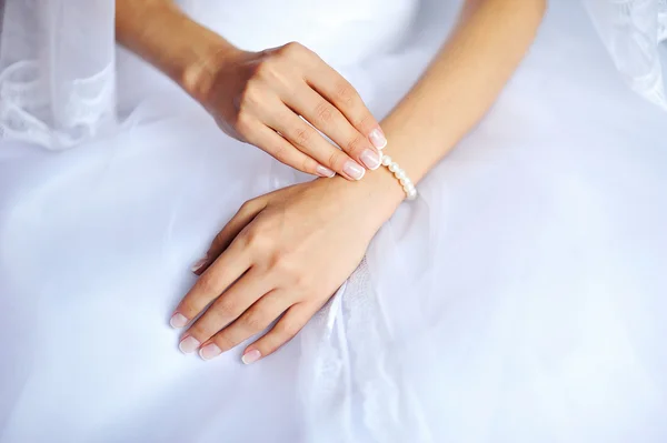 Mãos de noiva com manicure no vestido de casamento branco — Fotografia de Stock