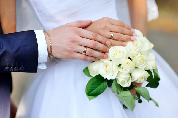 Ruce nevěsty a ženicha na bílé svatební kytice — Stock fotografie