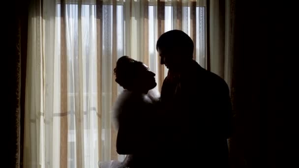 Силуэты жениха и невесты на фоне окна — стоковое видео