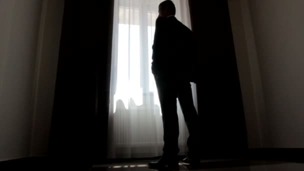 Silhouette of stylish man in suit looking out the window — Stock Video