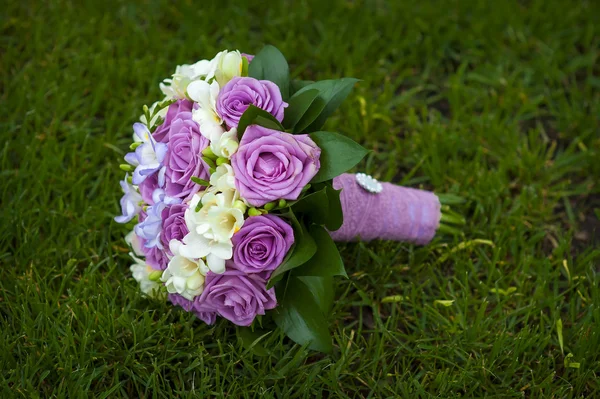 Buquê de casamento de rosas roxas e brancas deitadas na grama — Fotografia de Stock