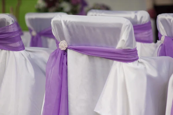 Beautiful white wedding chairs decorated with purple bows — Stock Photo, Image