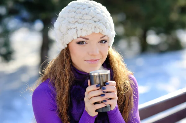 Schönes Mädchen, das auf einer Bank mit einer Tasse Kaffee sitzt. Winter — Stockfoto