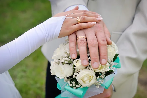 Main la mariée et le marié avec des anneaux sur le bouquet de mariage — Photo
