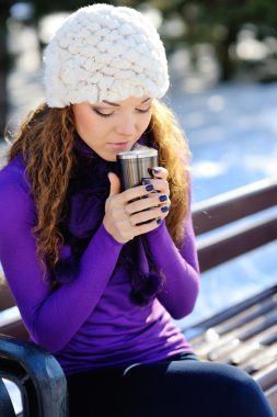 Kışın kahve ile bir bankta oturan beyaz şapkalı güzel kız