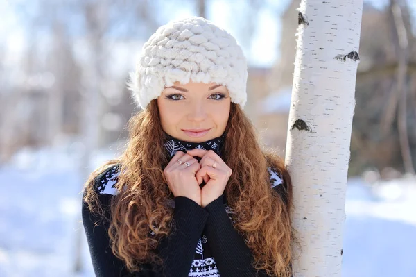 Linda morena em um chapéu branco em pé em um parque perto de uma árvore no inverno — Fotografia de Stock