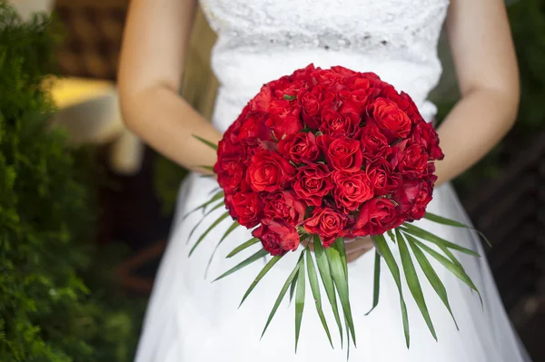 Wedding bouquet van rode rozen en bladeren in de hand van de bruid — Stockfoto