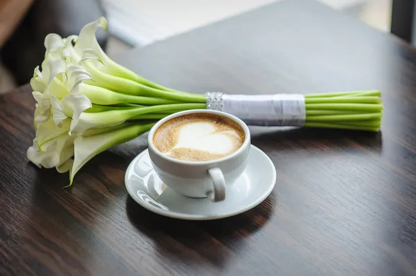 Ramo de boda de lirios de cala en una mesa con una taza de café —  Fotos de Stock