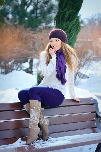 Young beautiful girl sitting on the bench in winter forest — Stock Photo, Image