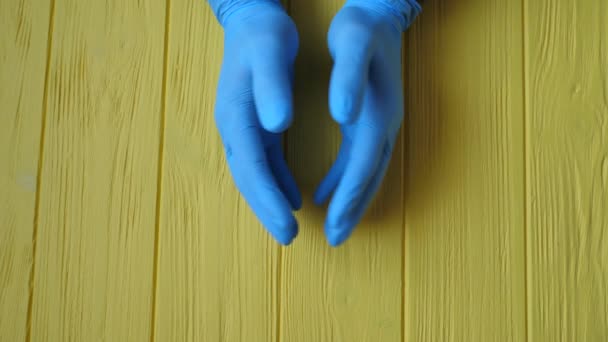 Doctor manos masculinas en guante azul estéril sobre un fondo de mesa de madera amarillo. Movimiento de vídeo 4K con lugar para texto — Vídeos de Stock