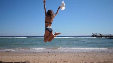 Kumsalda zıplayan mutlu kadın. Mutluluk ve başarı konsepti videosu. Yavaş çekimde sevinçten zıplayan genç bir kadının silueti.