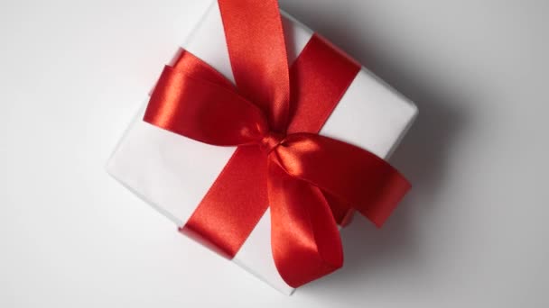 Rotate white gift box with red ribbon on white background with place for your text. Video motion on Valentines Day, mothers day or Birthday. Top view 4k footage — Vídeo de Stock