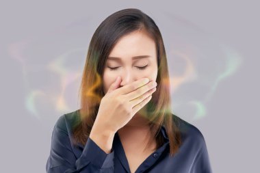 Asyalı bir kadın gece elle nefes testi yapıyor. Mavi elbiseli Asyalı kadının nefesi kokuyor. Ağız kokusu