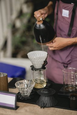 Kahve makinesi ve su ısıtıcısının üzerine dökülen kimyasallarla kahve hazırlayan profesyonel barista.