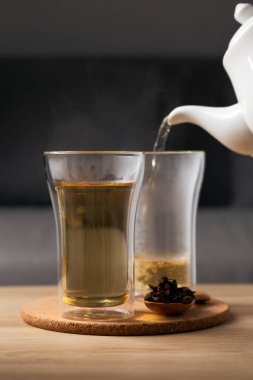 Tahta bir masaya yerleştirilmiş bardağa sıcak cascara çayı döküyorum..