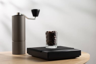 Dark roasted coffee beans in a clear glass on a digital scale and a Manual coffee grinder