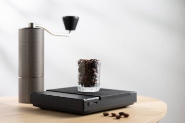 Dark roasted coffee beans in a clear glass on a digital scale and a Manual coffee grinder