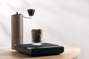Dark roasted coffee beans in a clear glass on a digital scale and a Manual coffee grinder