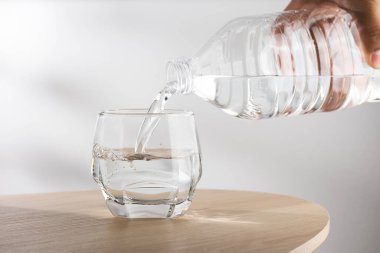 Man's hand holding drinking water bottle and pouring water into glass on wooden table clipart