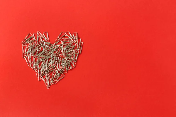 Kırmızı arka planda bir kalp. Sevgililer Günü. Sevgililer Günü tebrik kartı. Ataçların kalbi. Kırtasiye.