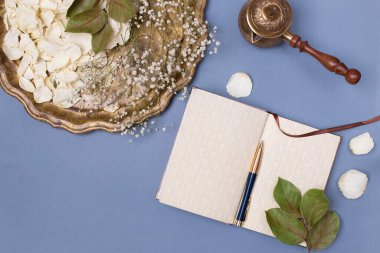 Beyaz gül yaprakları olan klasik tepsi manzarası, mavi arka planda boş günlük. Düz yatış, metin için yer.