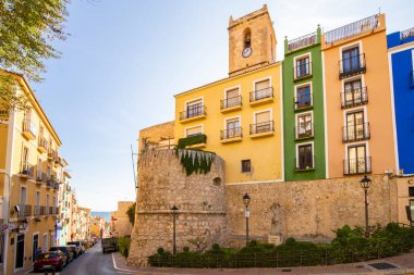 Villajoyosa, Costa Blanca, İspanya - 27 Kasım 2019: Taş kale duvarındaki renkli evler ve eski şehrin kulesi