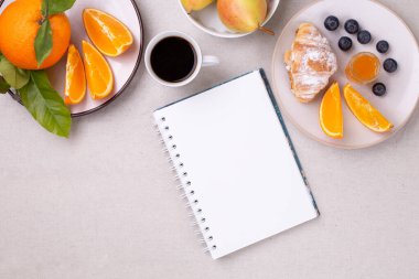 Boş günlük ve bir fincan kahve, taze kruvasan, reçel, olgun yabanmersini ve sulu portakallar beyaz arka planda, düz yerde, kopyalama alanı