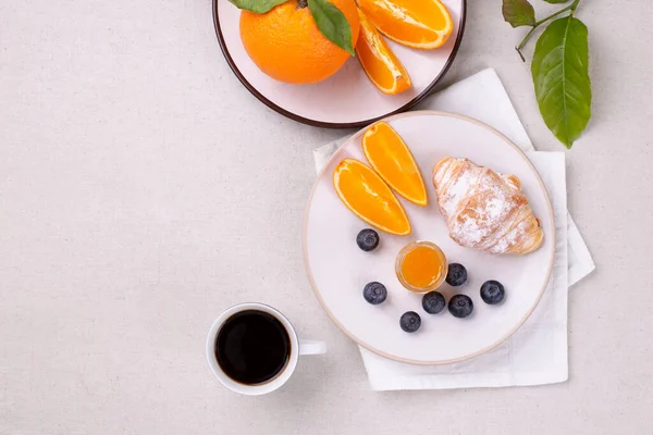 Café da manhã com uma xícara de café, croissant fresco, compota e mirtilos maduros e laranjas suculentas, em uma mesa branca, flat lay, espaço de cópia Imagem De Stock