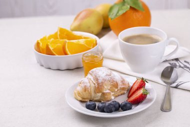 Bir fincan kahve, taze kruvasan, olgun çilek ve yaban mersini ve hafif bir masada sulu portakal dilimleri ile kahvaltı..