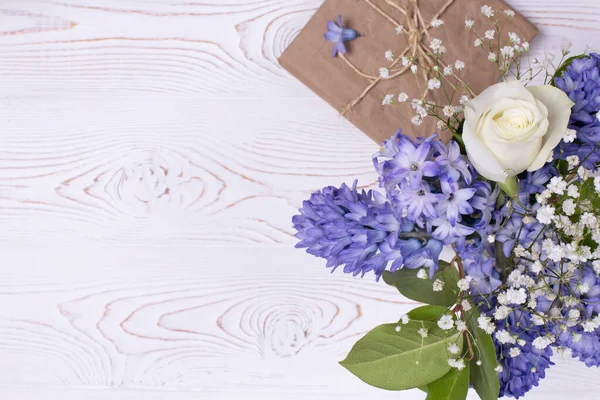 Una confezione regalo avvolta in carta artigianale e fiori di giacinto blu, rose bianche su un piano d'appoggio bianco. Piatto. Copia spazio per testo Foto Stock Royalty Free