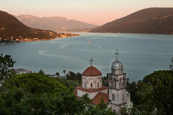 Mosteiro de Savina - Mosteiro ortodoxo sérvio no contexto de uma cordilheira e da Baía de Kotor ao pôr-do-sol, a cidade de Herceg Novi, Montenegro. Imagem De Stock