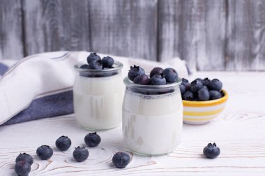 Cam kavanozlarda Yunan yoğurdu ve kırsal beyaz bir masada taze yaban mersini. Cam kavanoza odaklan