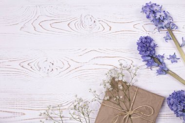 Bahar kompozisyonu, kraft kağıdı ve mavi sümbül çiçeklerine sarılı bir hediye kutusuyla beyazlatılmış bir masa üzerinde beyaz çingene. Metin için alanı kopyala