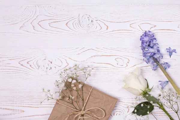 Composizione primaverile, Una confezione regalo avvolta in carta artigianale e fiori di giacinto blu, rose bianche su un piano d'appoggio bianco. Piatto. Copia spazio per testo — Foto Stock