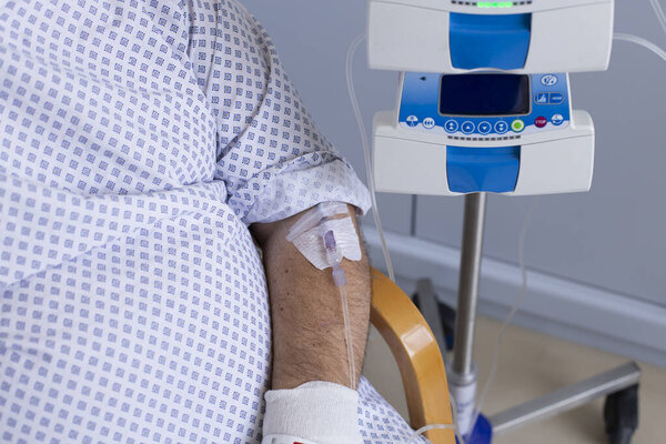 Человек с избыточным весом сидит в кресле с капельницей, оборудование на переднем плане, пациент в больнице.